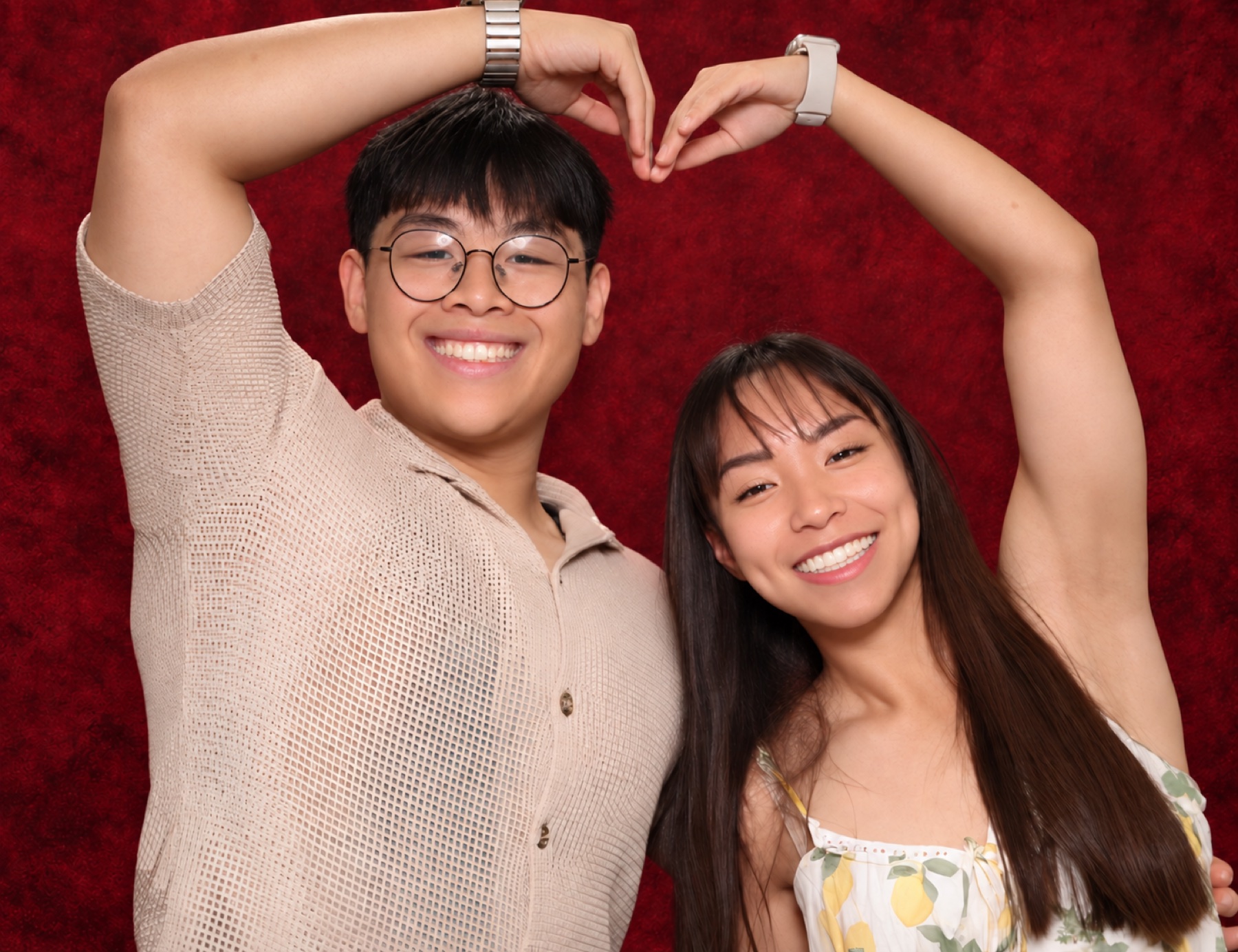 A smiling couple making a heart shape in front of the merlot backdrop